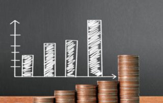 Steady Cash Flow: Image of a blackboard with a graph that slopes upwards. Stacks of coins sit on a desk next to the blackboard.
