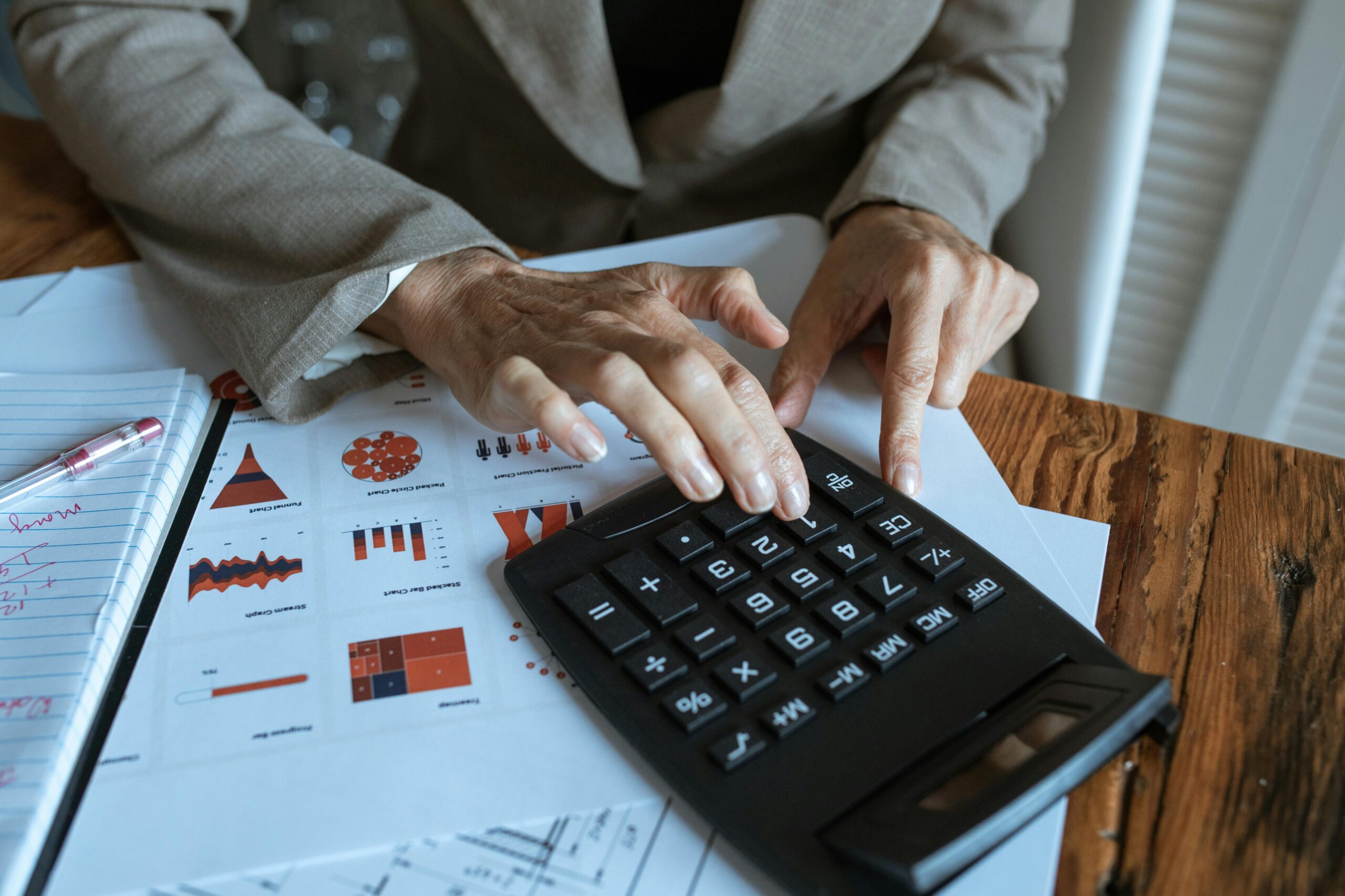 Close-up of a businessperson's hands using a calculator over financial charts, indicating meticulous budgeting and expense tracking.