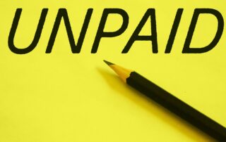 Unpaid Invoices: Close-up image of a pencil on yellow paper with the word "UNPAID" written on it.
