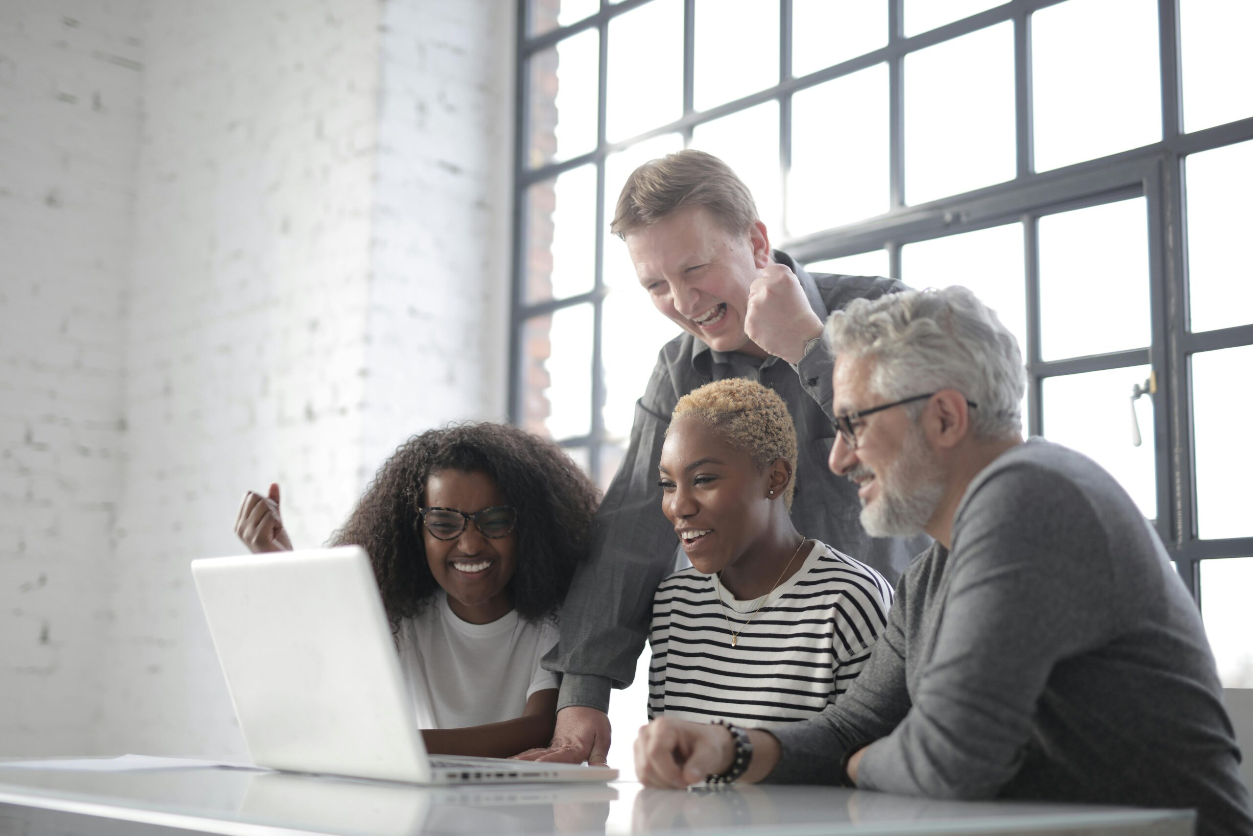 Diverse team of professionals joyfully discussing successful invoice strategies on a laptop in a modern office.