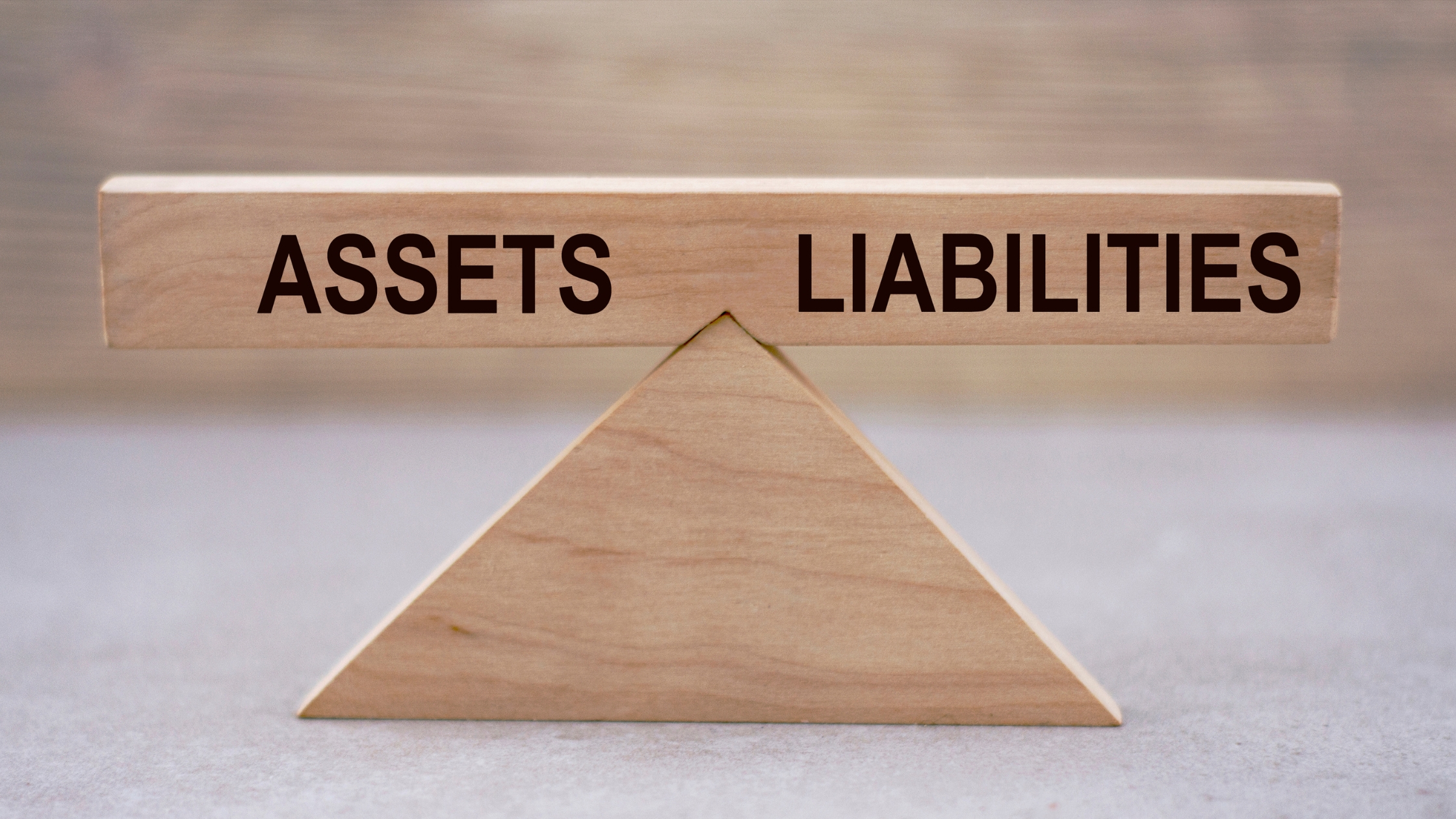 Wooden block divided into "Assets" and "Liabilities" sections, illustrating an Asset and Liability Report used in debt collection.