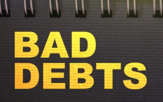 Close-up image of a notebook with the words "Bad Debts" handwritten on the page. This image is for a blog post about bad debt in construction.