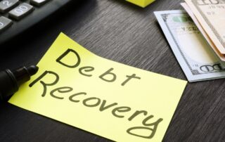 Sticky note with "Debt Recovery" written on it placed on a desk next to a calculator.