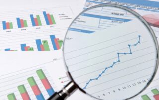 Asset and Liability Reports: A magnifying glass rests on top of a graph with vertical bars labeled "Income" and "Expenses". Text on the right side of the graph lists various expense categories.