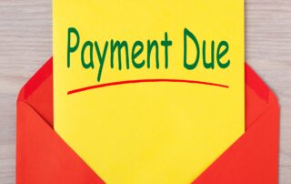 Close-up of red envelope containing yellow overdue payment notice on wooden desk.