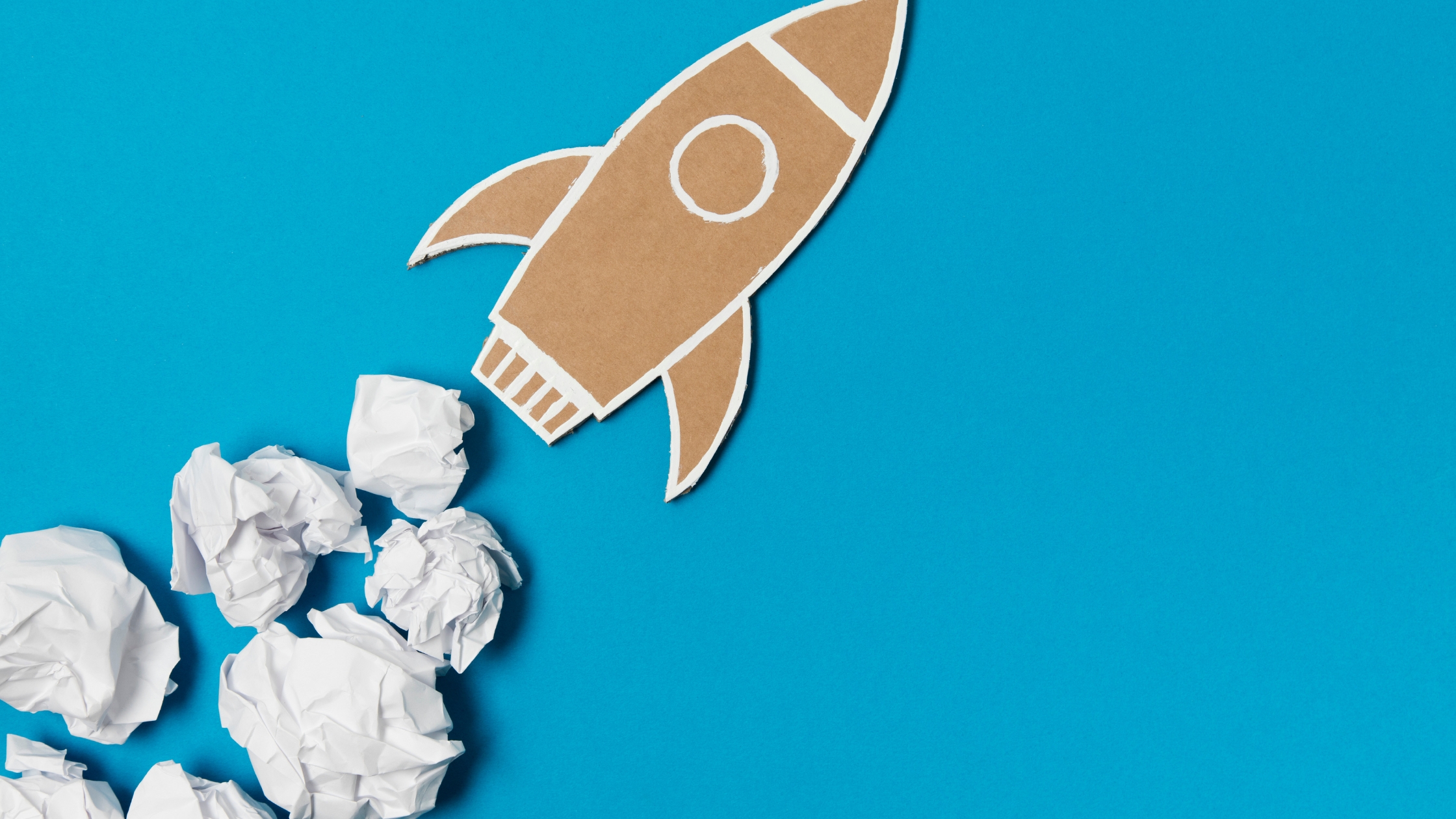 Collect Debt Faster: Cardboard rocket illustration flying through crumpled white paper clouds, symbolizing overcoming debt collection challenges. The Baker Group debt collection services.