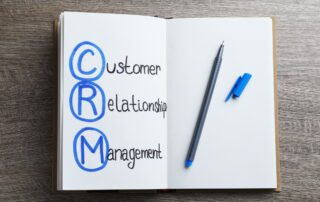 Bad Debt: Open notebook displaying "CRM" (Customer Relationship Management) with a blue pen, highlighting the significance of CRM in maintaining positive customer interactions and minimizing the risk of bad debt.