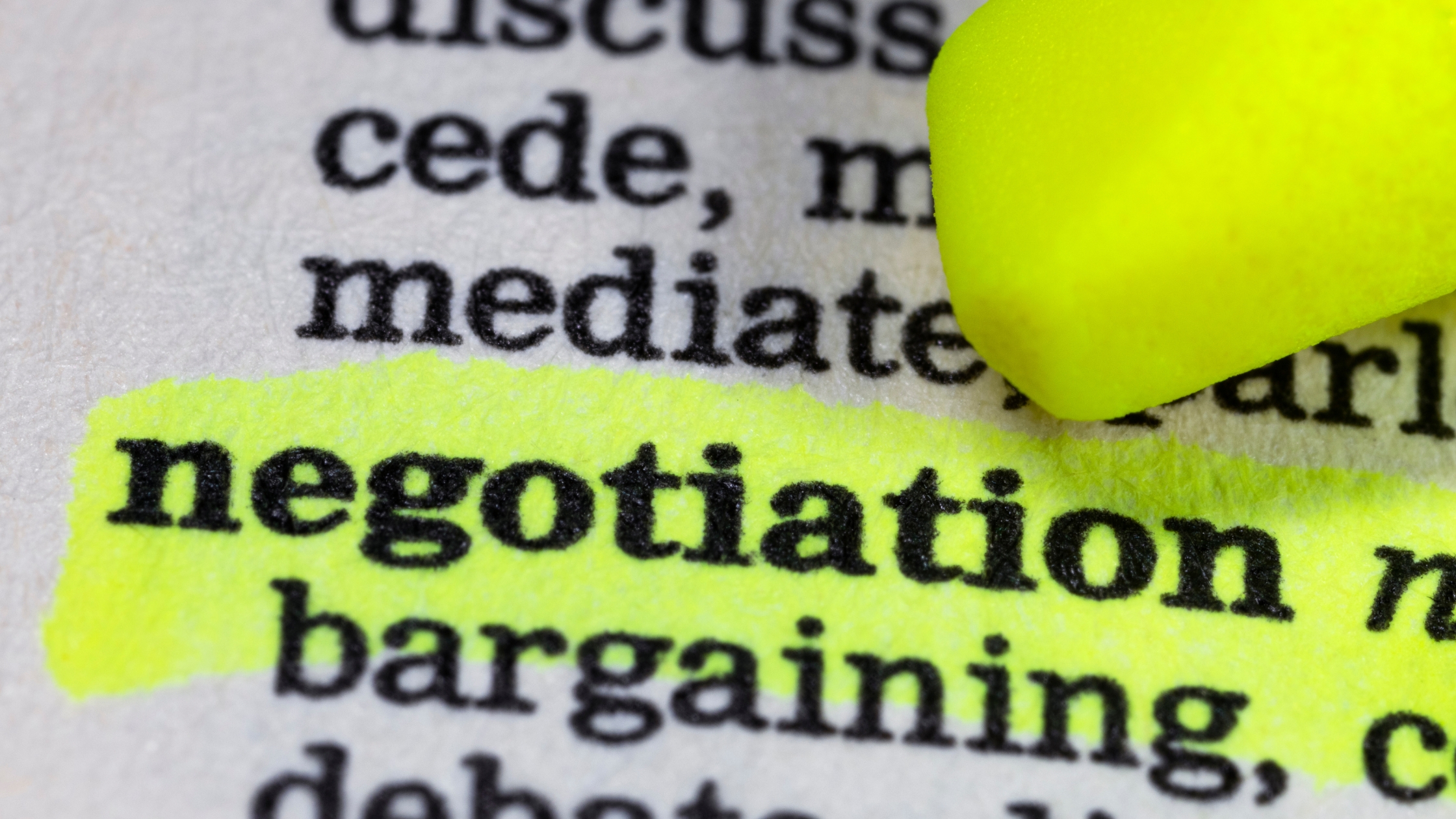 Navigating Debt Negotiation: Image of a dictionary open to a page with the word "negotiation" highlighted in yellow marker. Text around the highlighted word includes "cede," "mediate," "bargaining," and "concede." This image represents planning and research for debt negotiation.